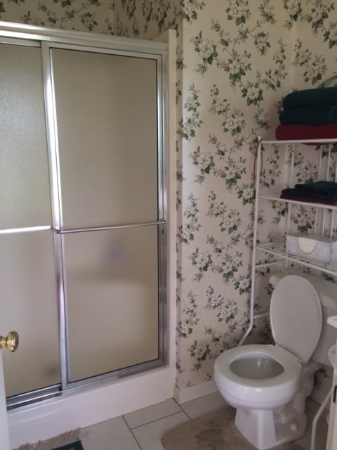 bathroom with shower insert wallpaper and shelf over toilet