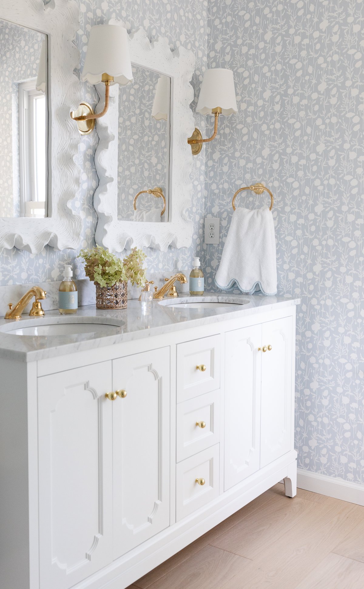 A soft blue and white wallpapered bathroom with a double white bathroom vanity.
