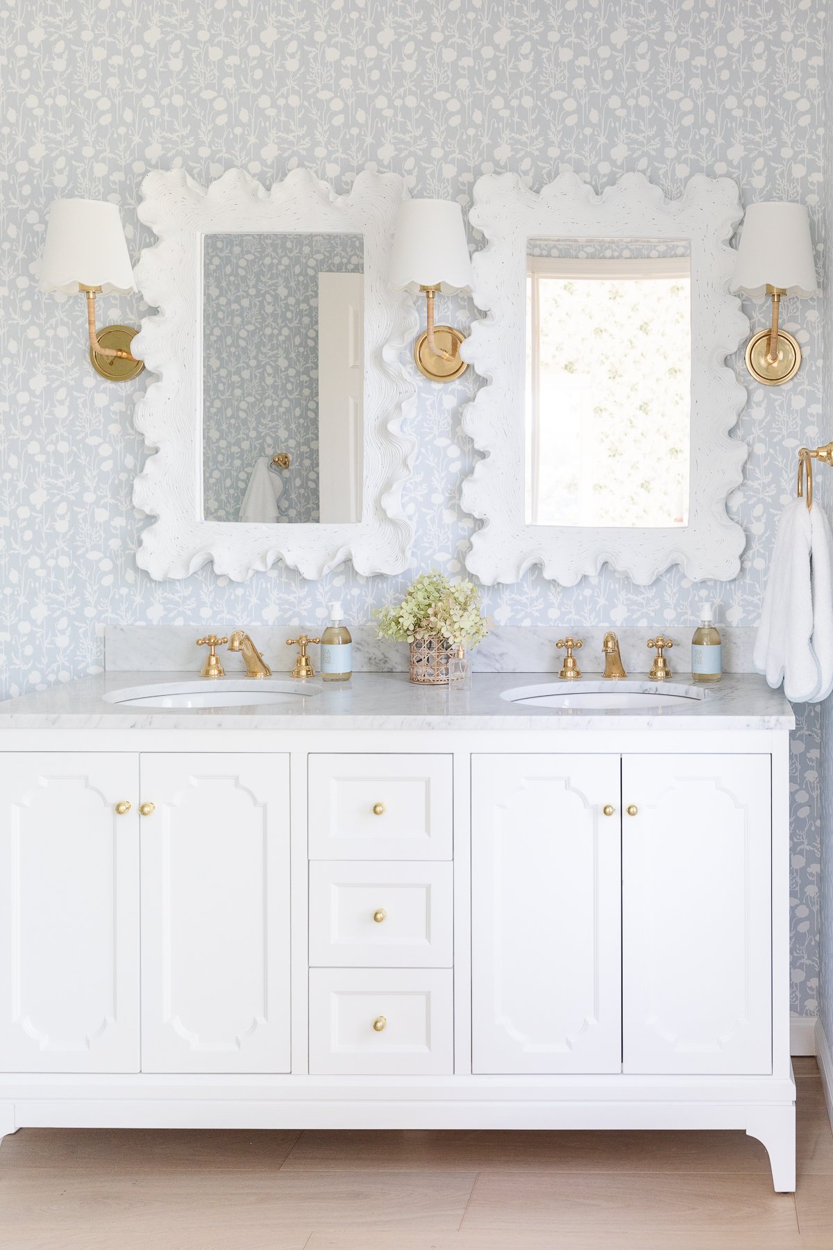 A soft blue and white wallpapered bathroom with a double white bathroom vanity.