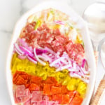 A grinder salad recipe in a white oval bowl, with rattan serving utensils to the side.