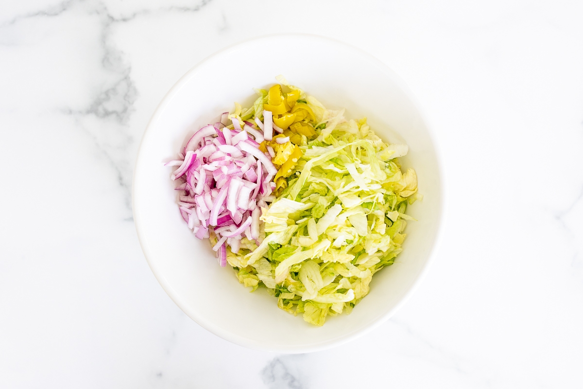 chopped lettuce, peppers and onions in a white bowl