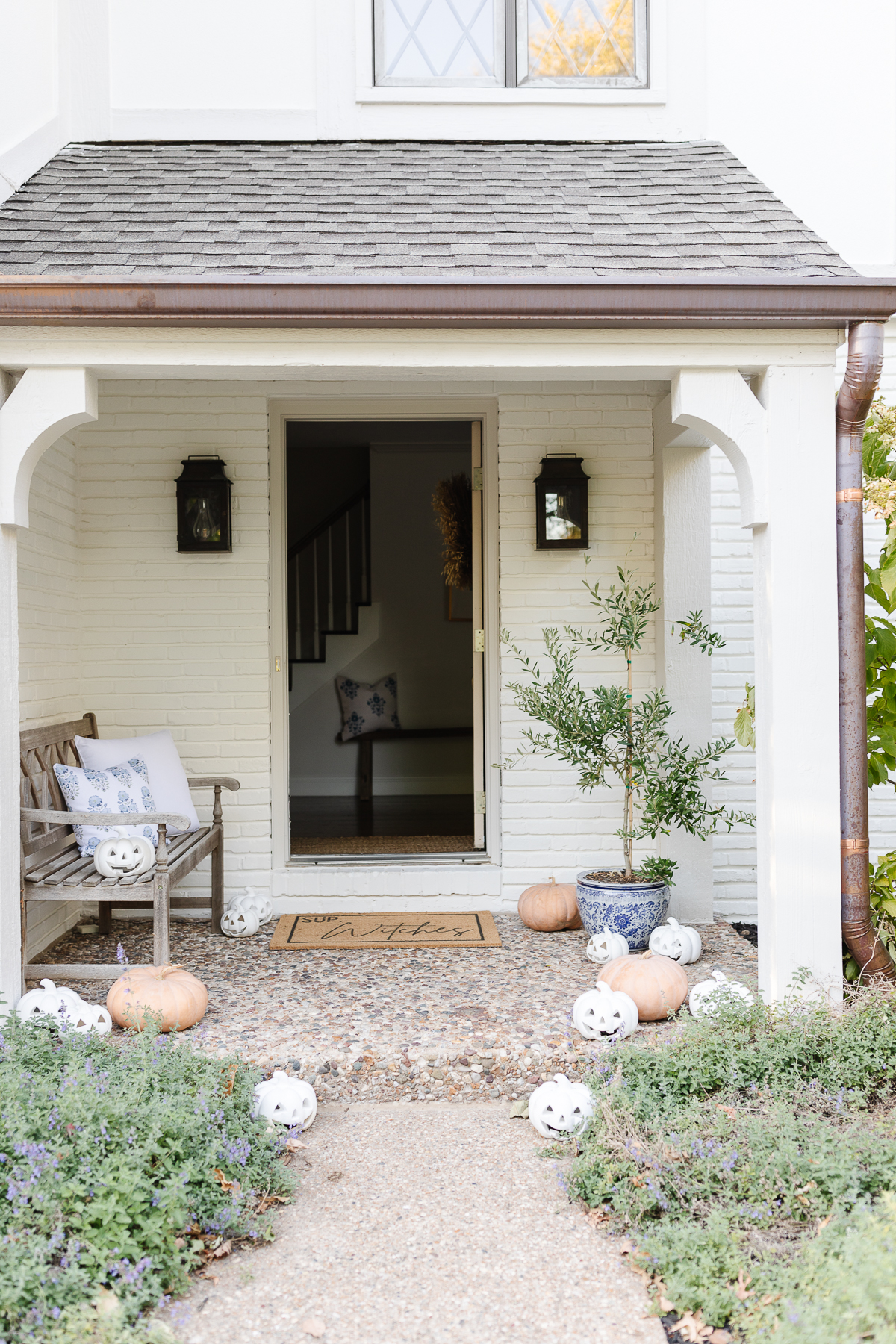 A white front porch with pumpkins and a bench.