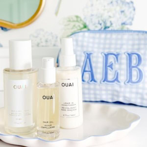 Three Ouai hair care products and a blue gingham monogrammed toiletry bag on a scalloped tray.