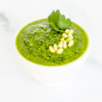 A white bowl of fresh pesto parsley on a white countertop.