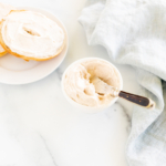 A bowl of cinnamon cream cheese and a bagel on a white table.