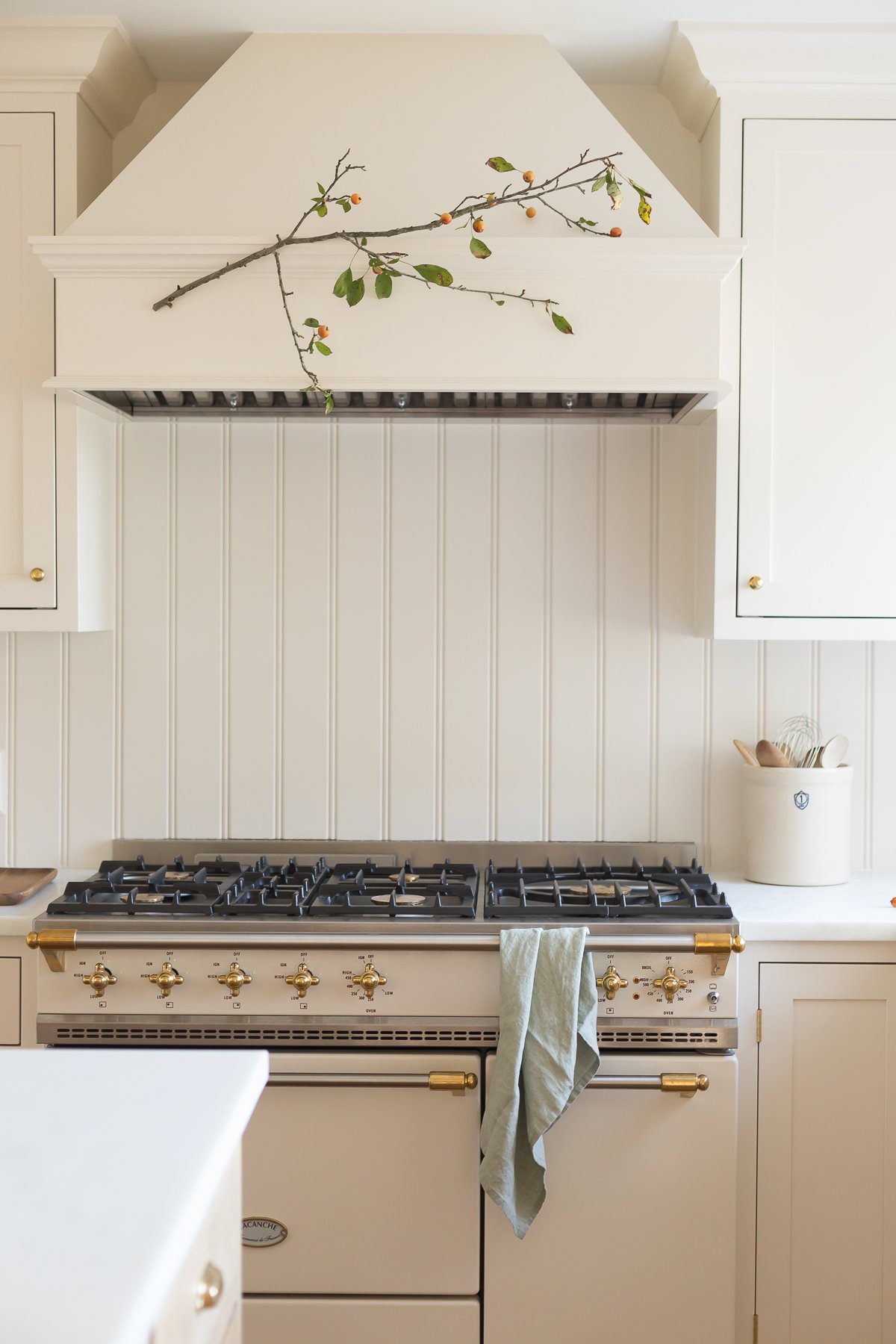 A white kitchen with fall branches hanging over the range.