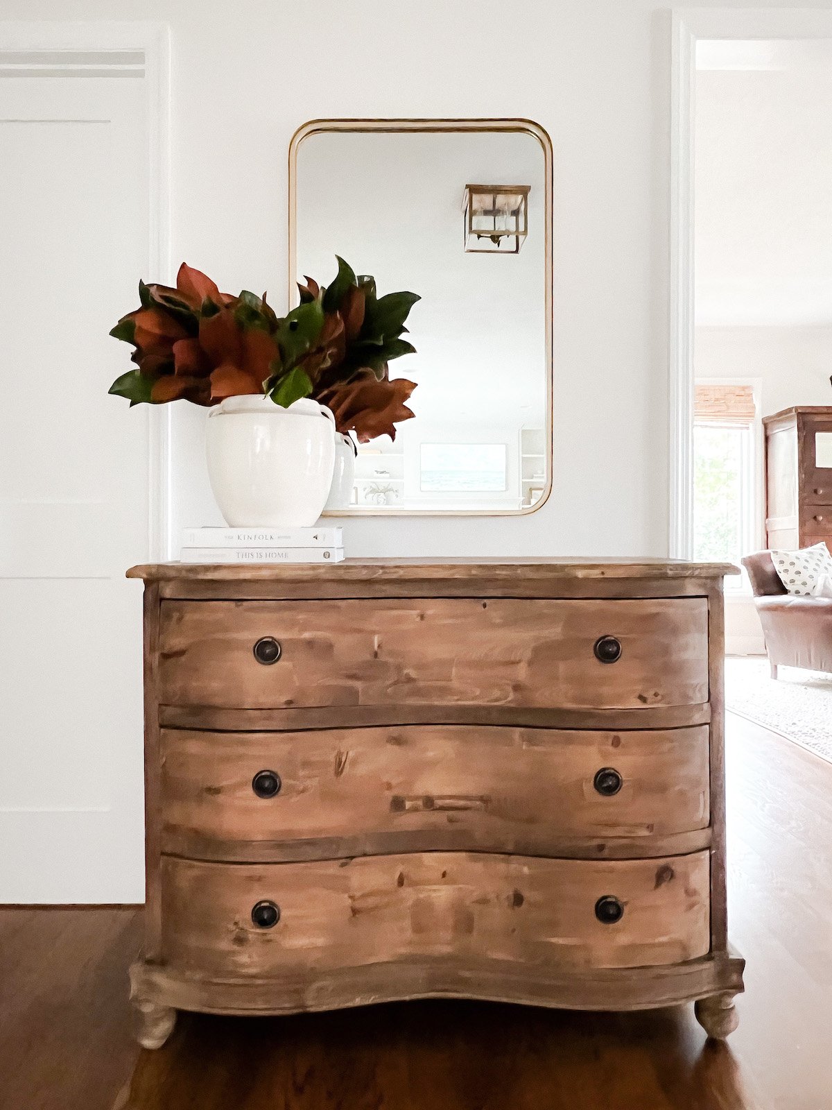 A wooden dresser with a mirror in the room decorated with fall branches.