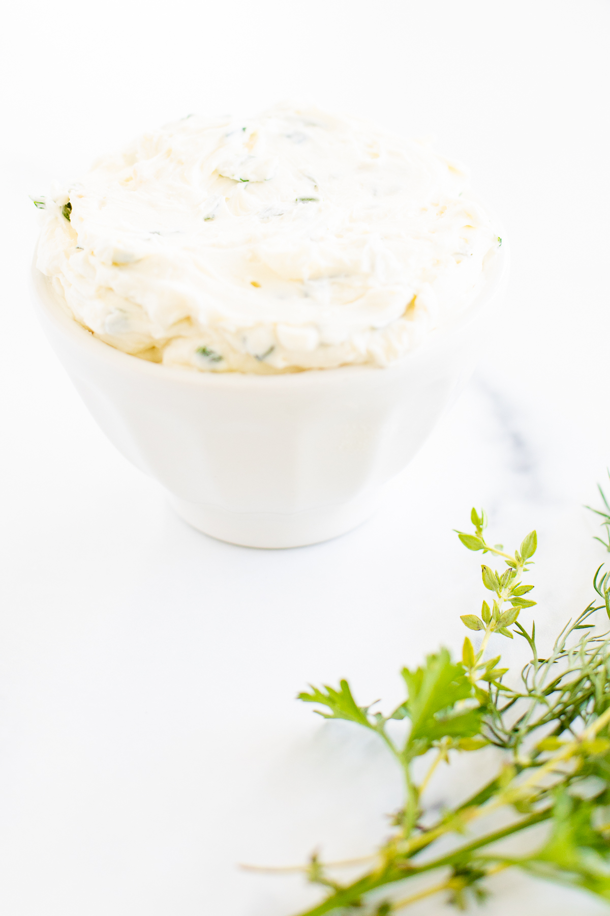 A white bowl of garlic and herb cream cheese on a marble countertop.