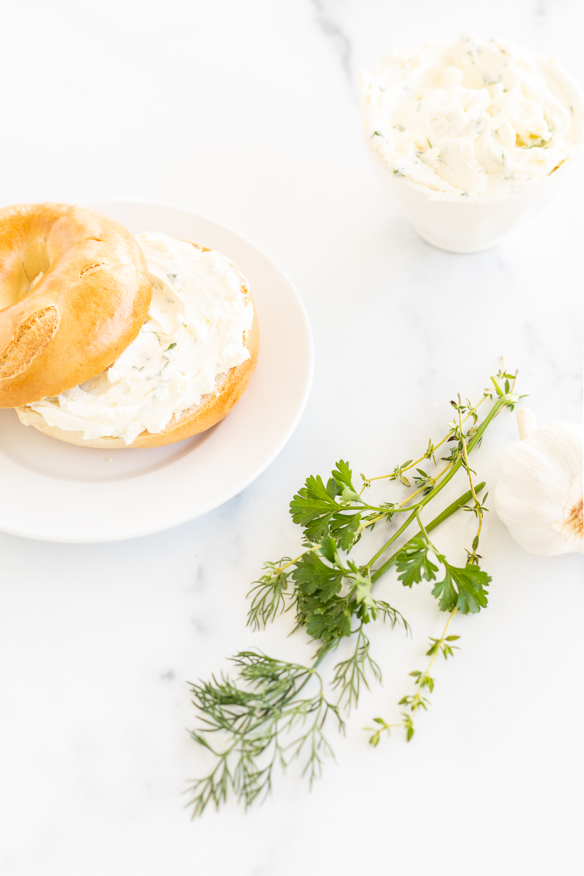 A bagel topped with garlic and herb cream cheese on a white plate. 