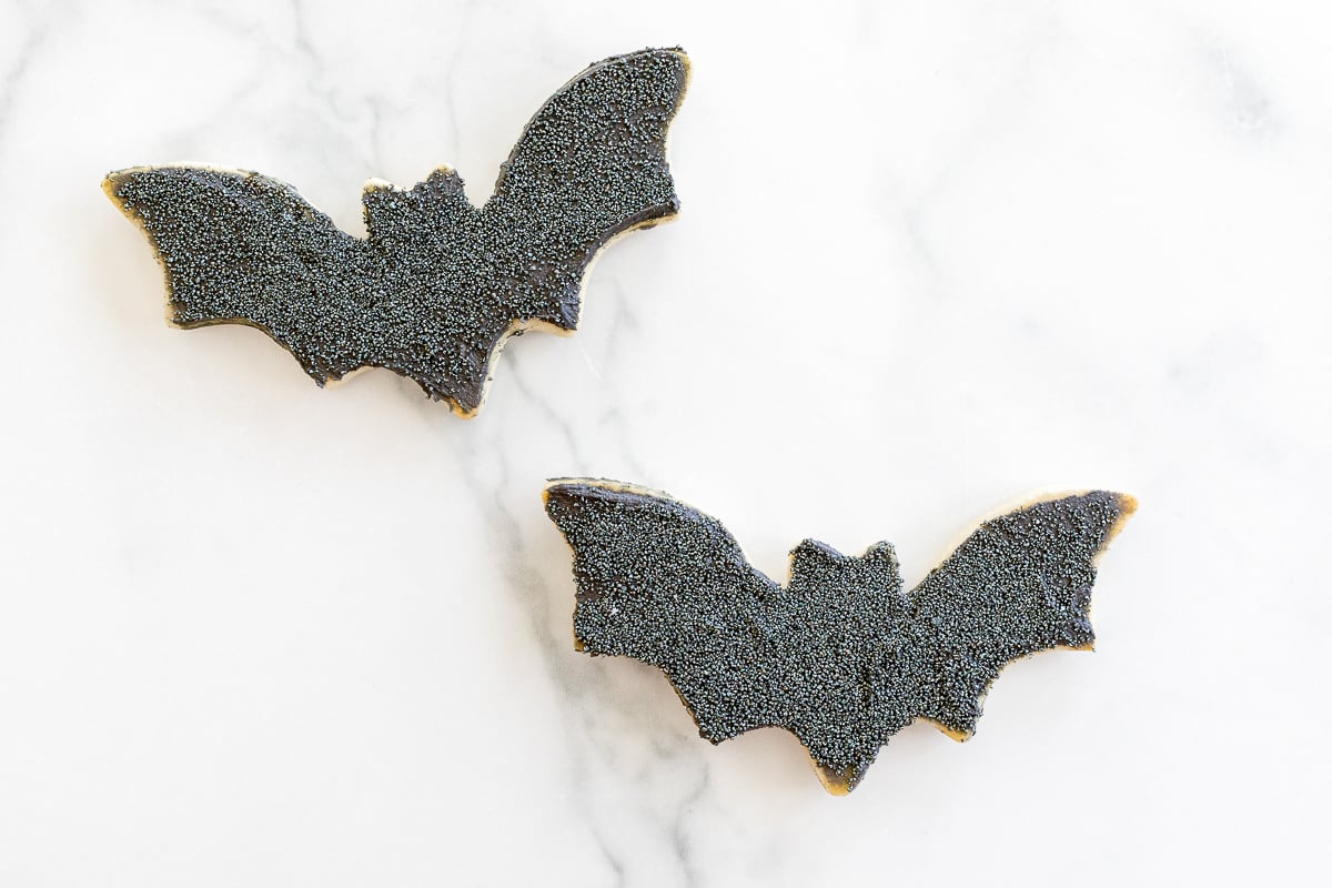 Two black bat Halloween sugar cookies on a white marble countertop. 