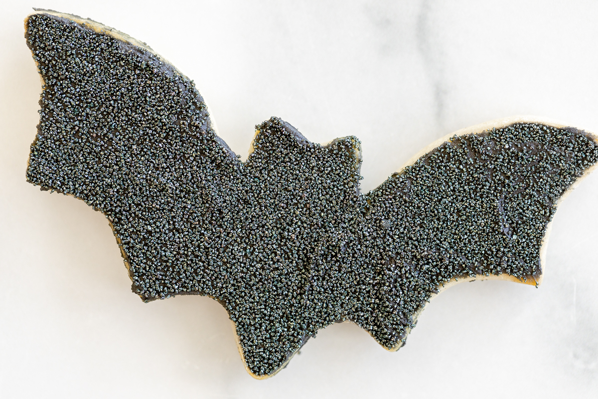 Black bat Halloween sugar cookie on a white marble countertop.