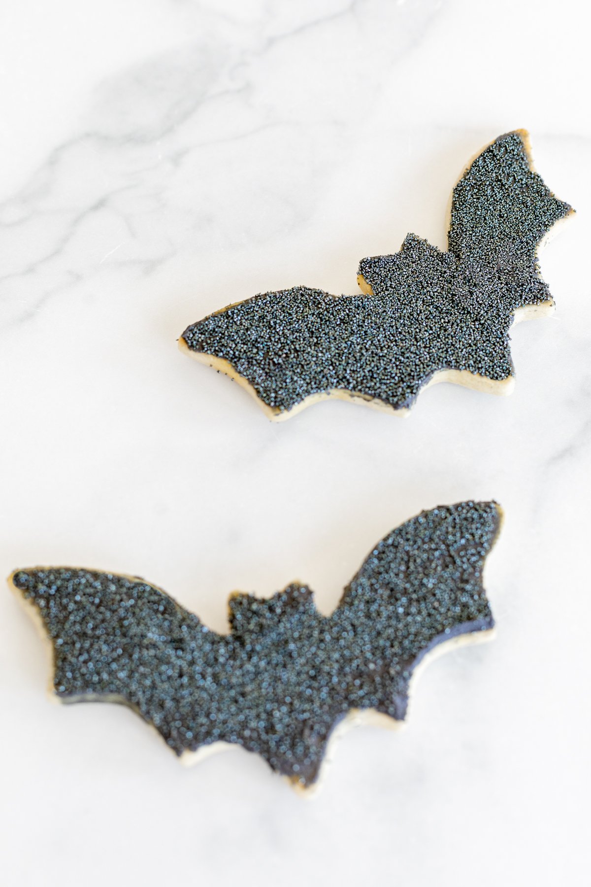 Two black bat Halloween sugar cookies on a white marble countertop.