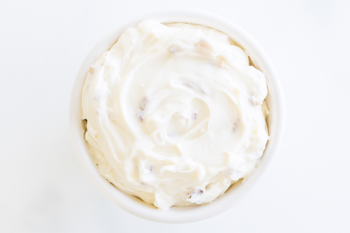 A white bowl of honey walnut cream cheese on a white surface.