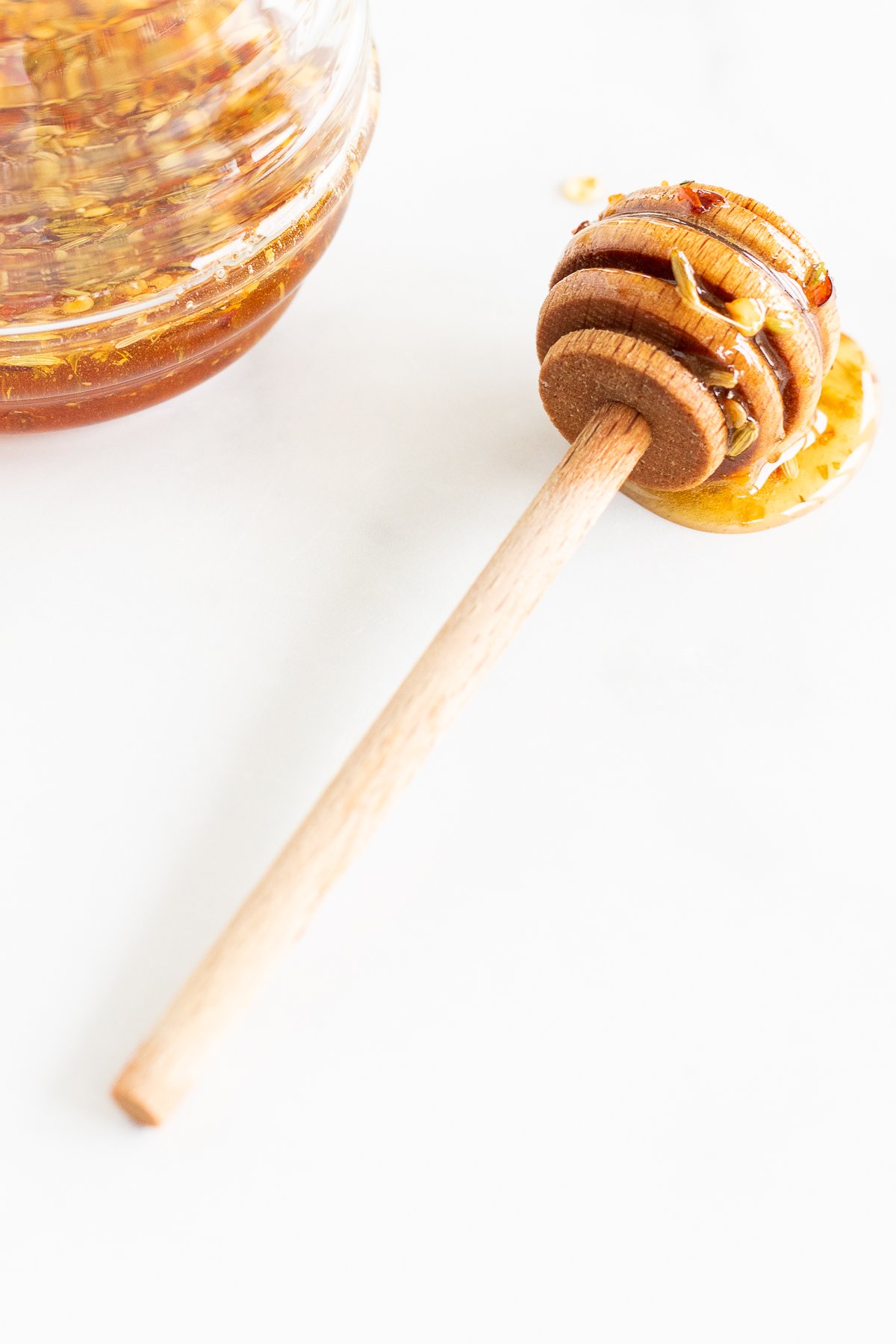 A wooden spoon with honey on it next to a glass jar of hot honey.
