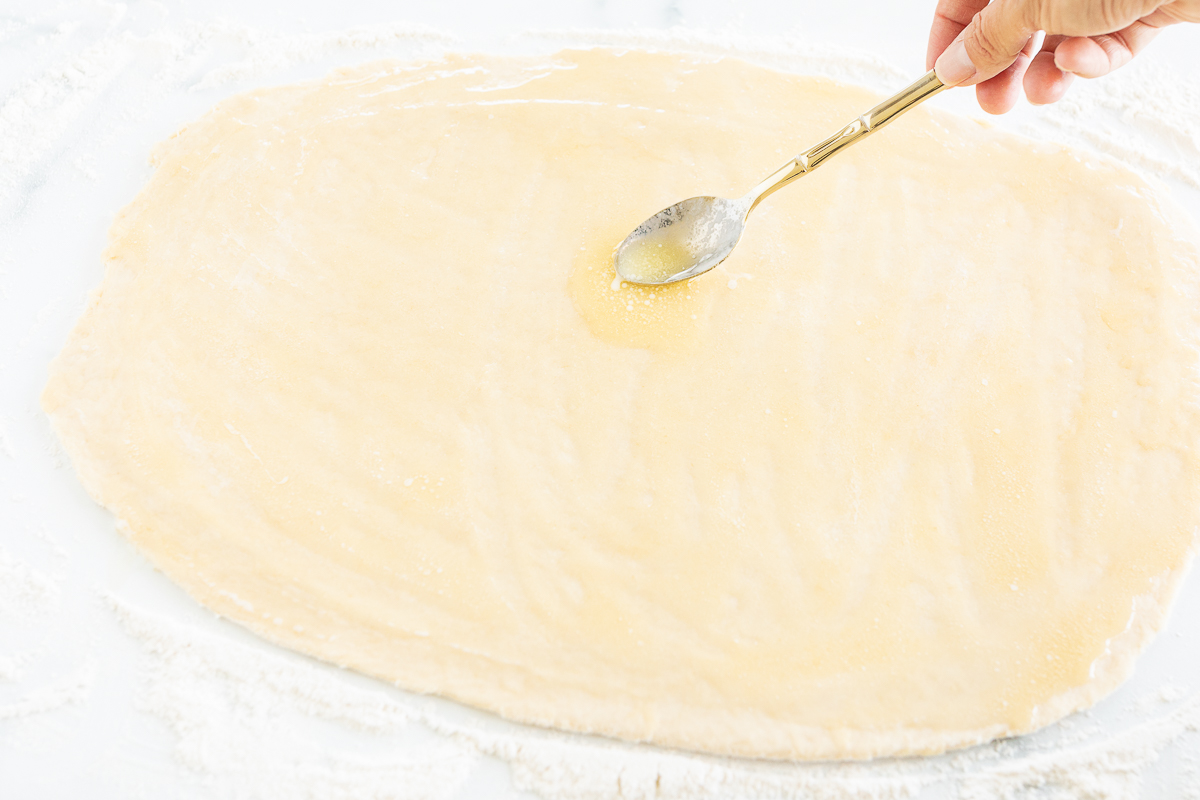 Making apple cinnamon rolls, a person delicately pours a spoonful of flour onto the dough.