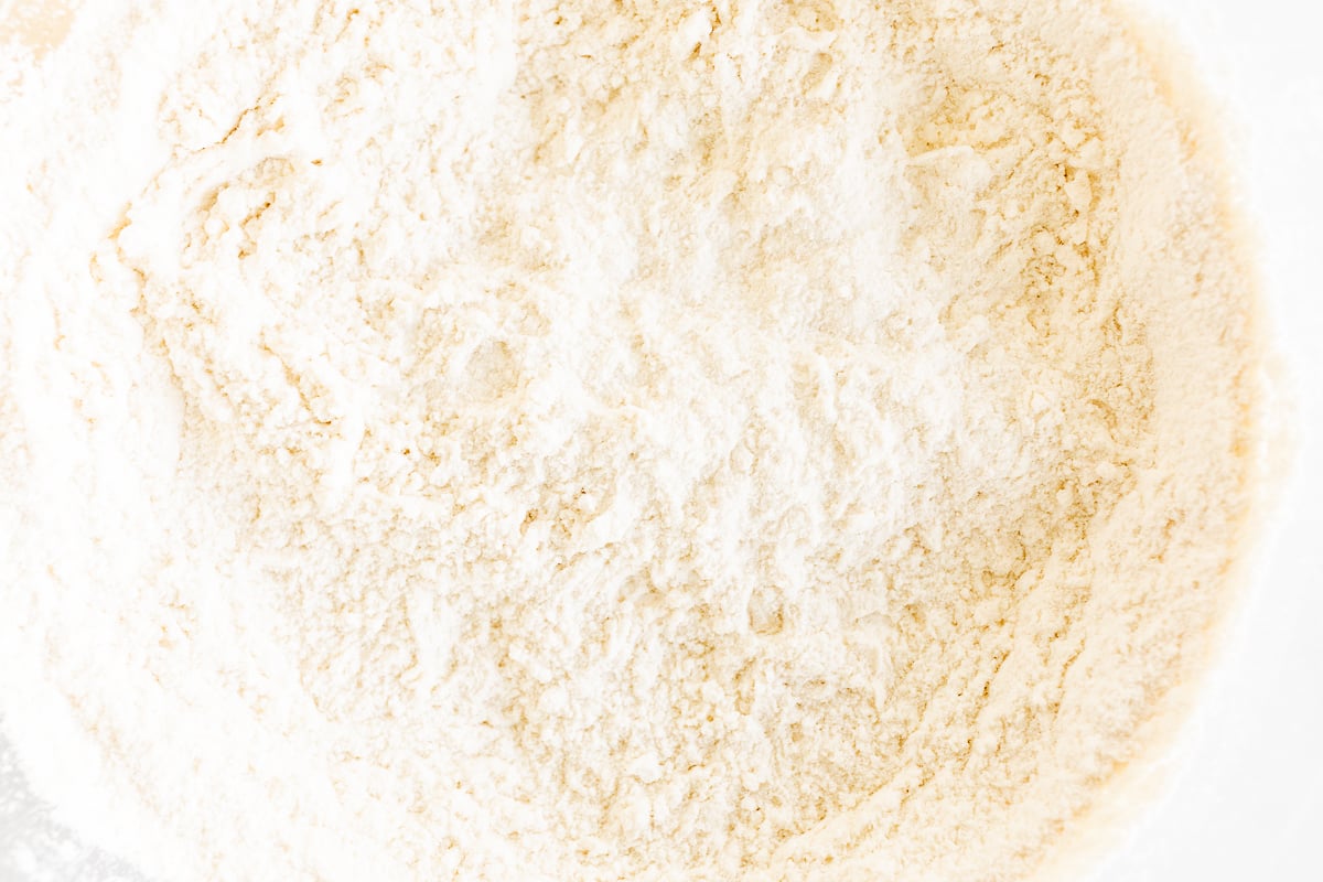 A bowl full of flour on a white surface, perfect for making apple cinnamon rolls.