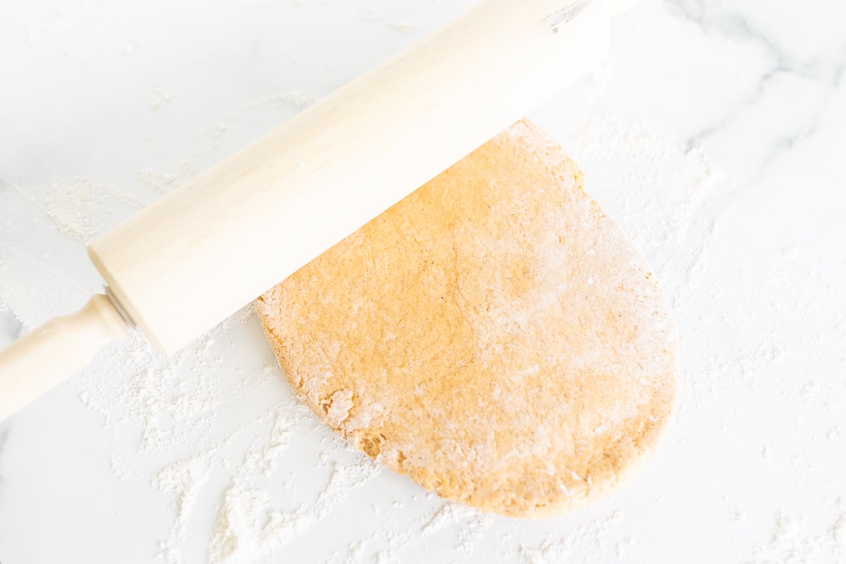 A rolling pin with flour on top of a dough for making pumpkin cinnamon rolls.