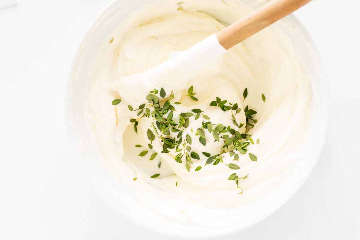A bowl of whipped ricotta with herbs and a wooden spoon.