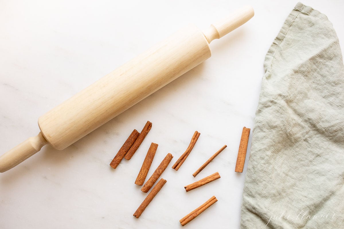 A rolling pin and cinnamon sticks on a marble table.
