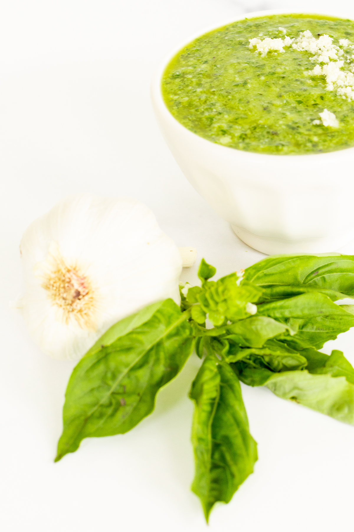 A bowl of nut-free green soup next to a bowl of garlic.