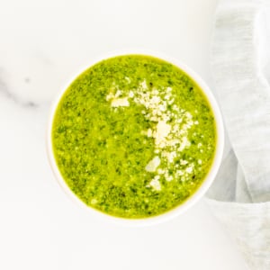 A bowl of green Nut Free Pesto soup on a white table.
