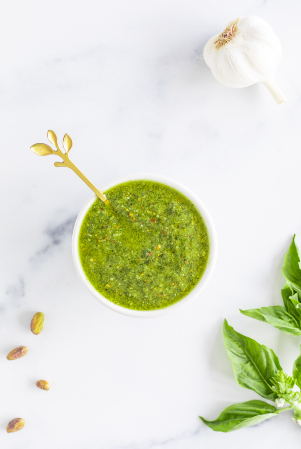 Pistachio pesto sauce in a white bowl with basil and garlic.