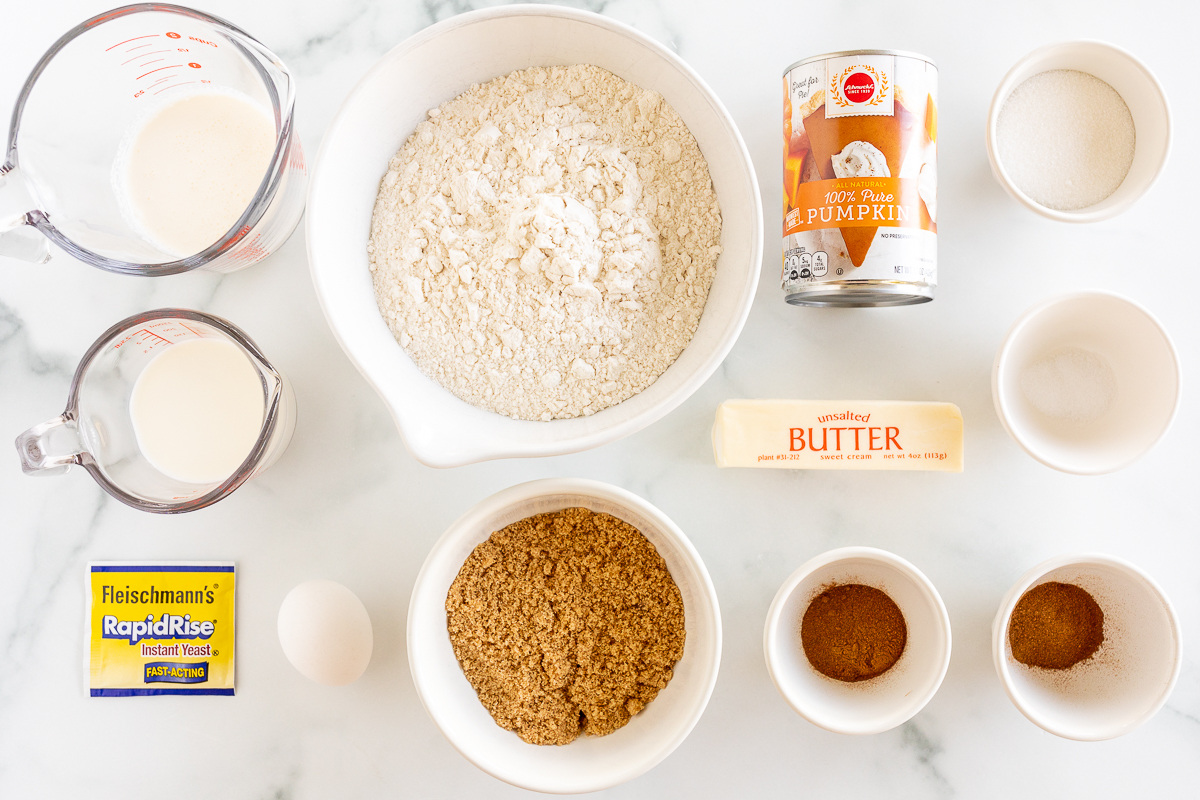 The ingredients for a Pumpkin Cinnamon Rolls are laid out on a marble table.