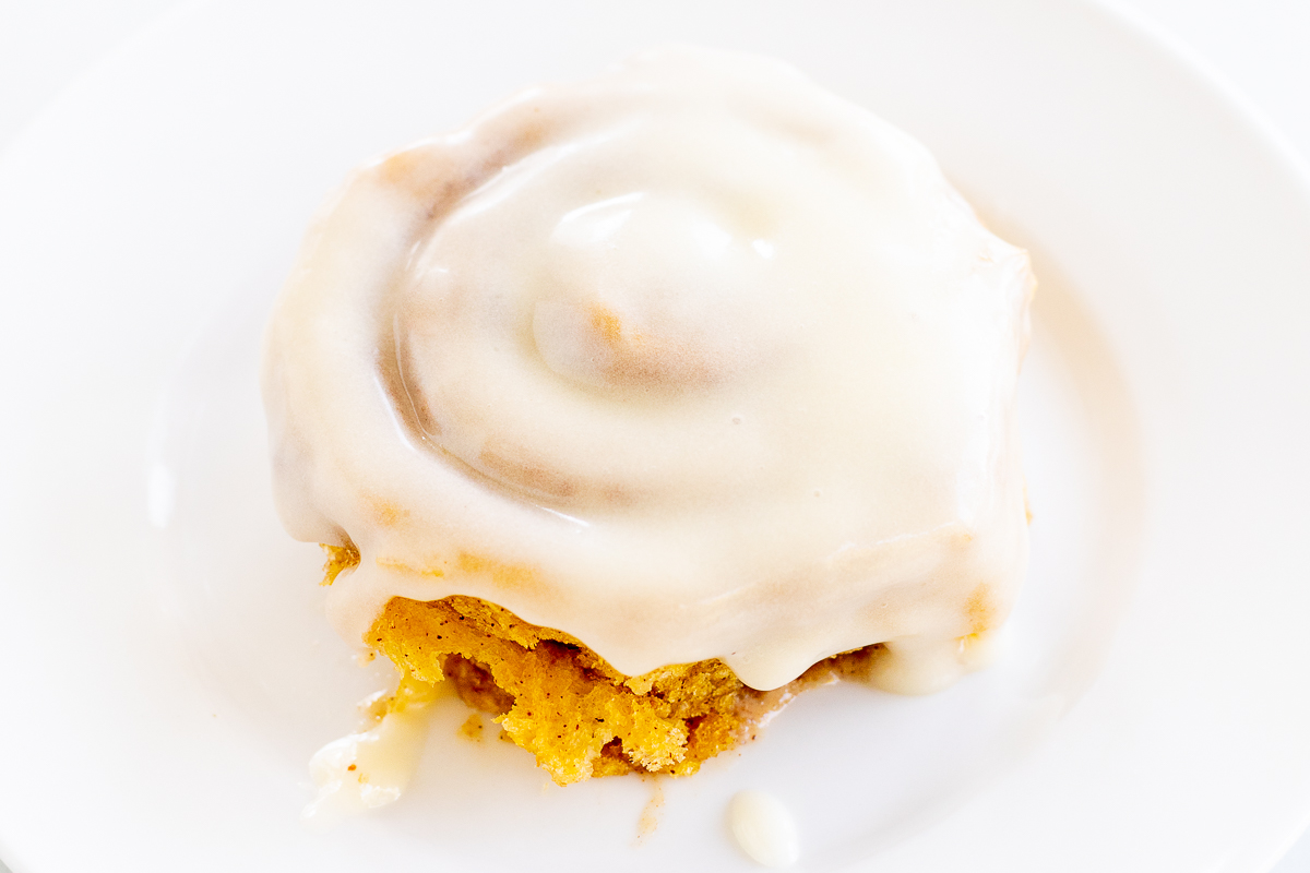 Pumpkin Cinnamon Rolls with icing on a white plate.