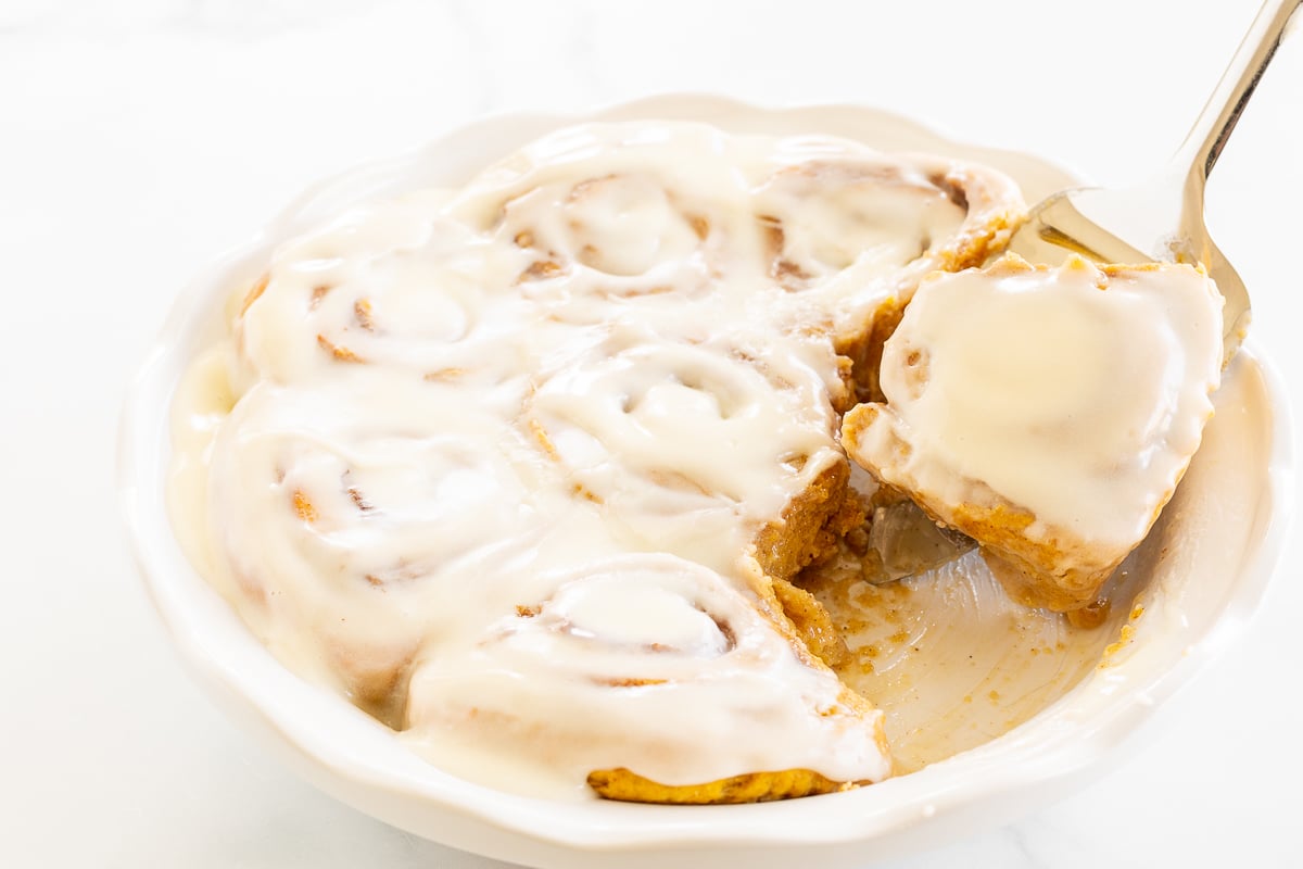 A bowl of pumpkin cinnamon rolls with icing and a spoon.