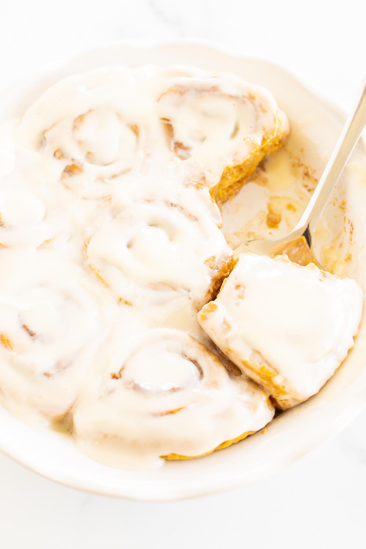Pumpkin cinnamon rolls in a white bowl with icing.