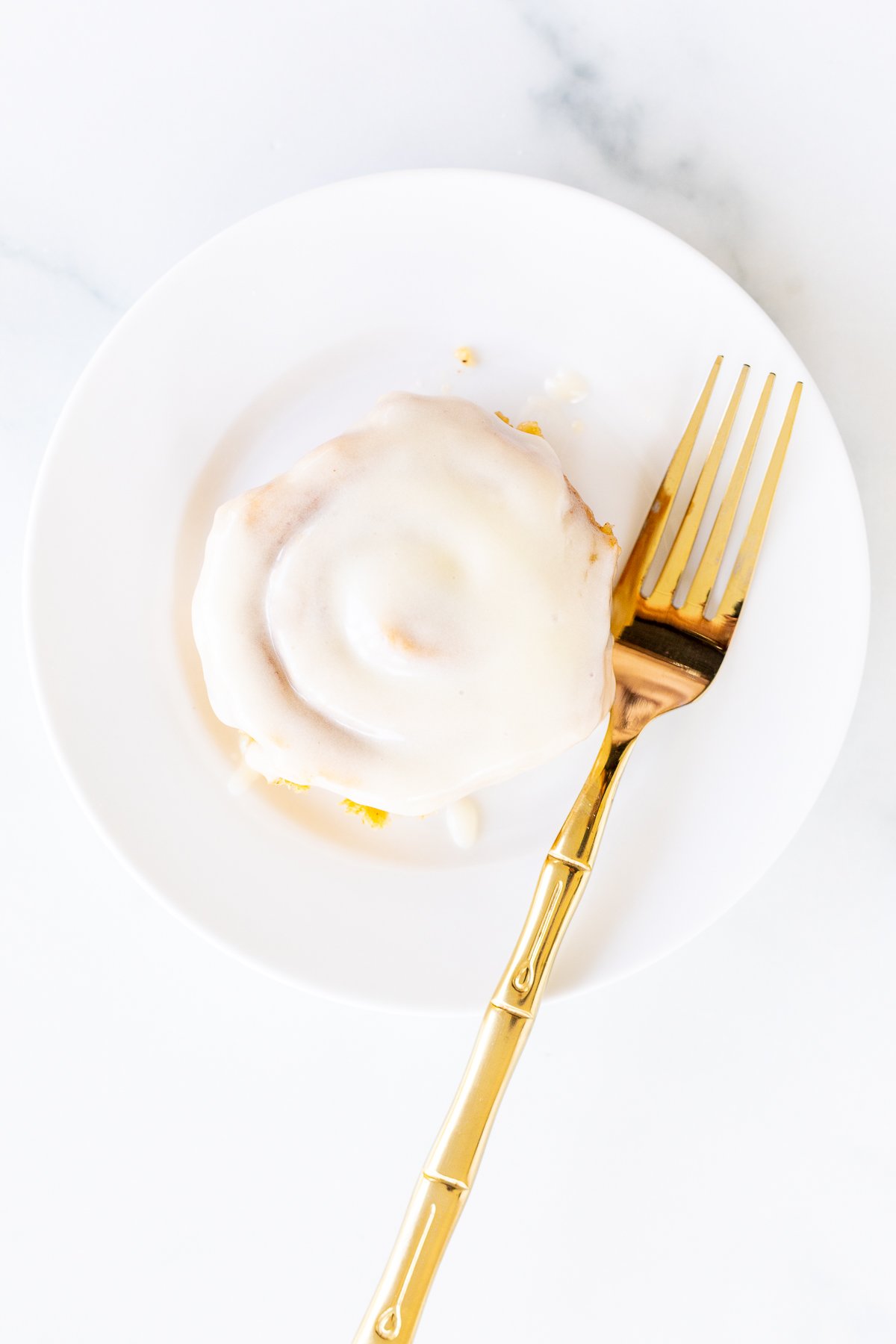 A pumpkin cinnamon roll on a white plate with a gold fork.