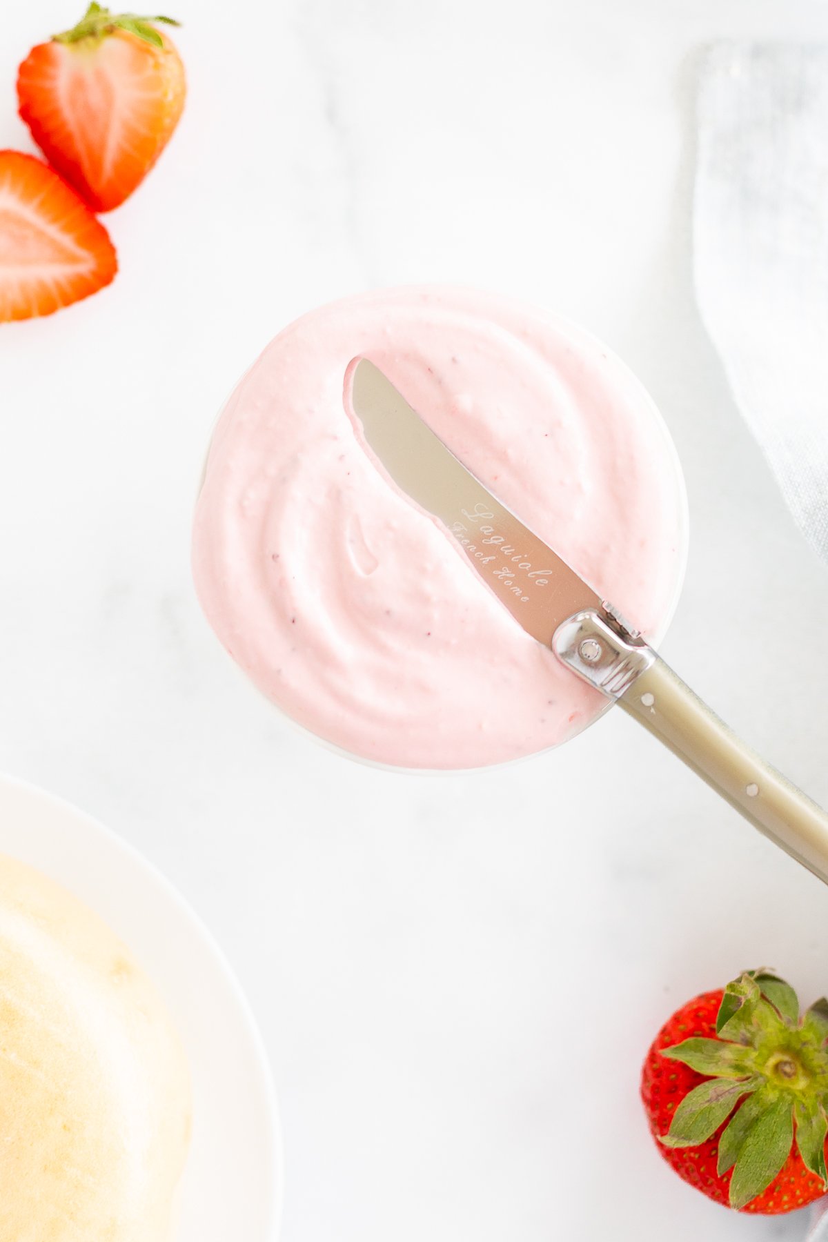 A knife on top of a bowl of strawberry cream cheese. 