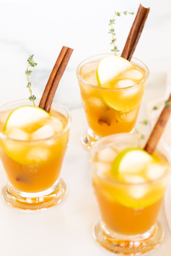 Three glasses of apple cider with cinnamon sticks, perfect as Thanksgiving drinks.
