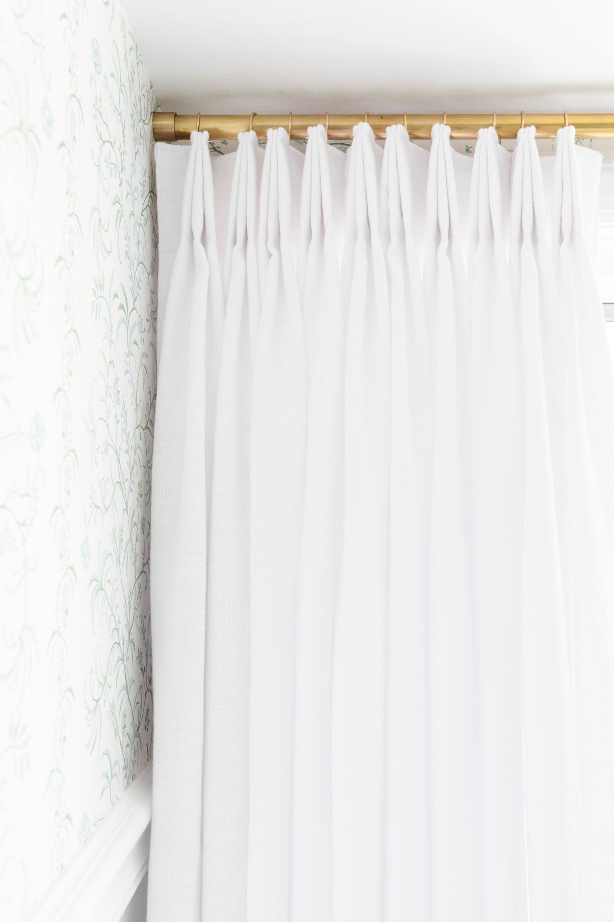 Pinch Pleat Drapes hang on a gold rod in a room.