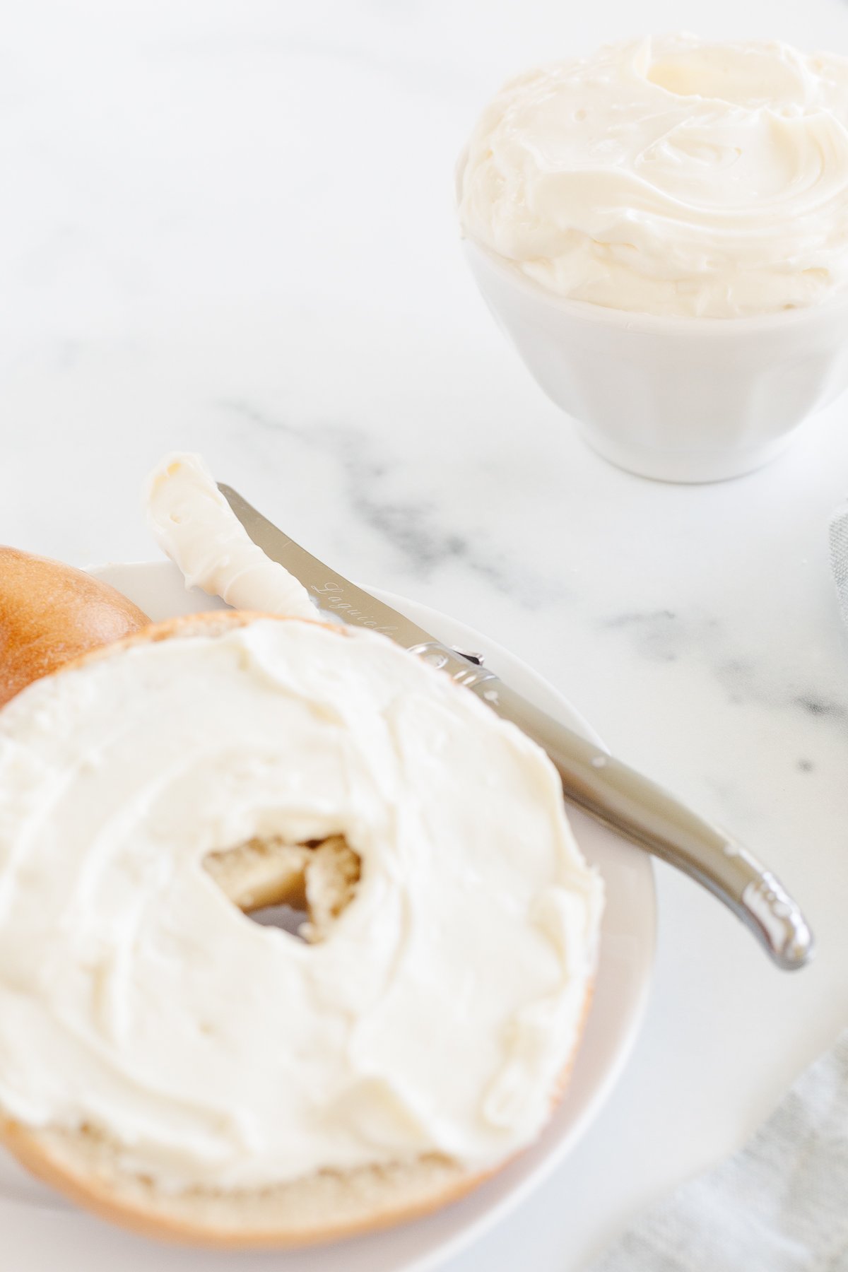 A bagel with whipped cream cheese and a knife next to it.