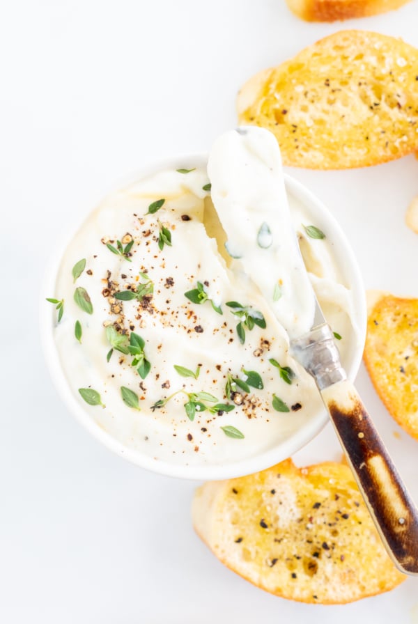 A bowl of whipped ricotta dip with bread and herbs.