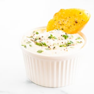 A cup of dip with a cracker on top.