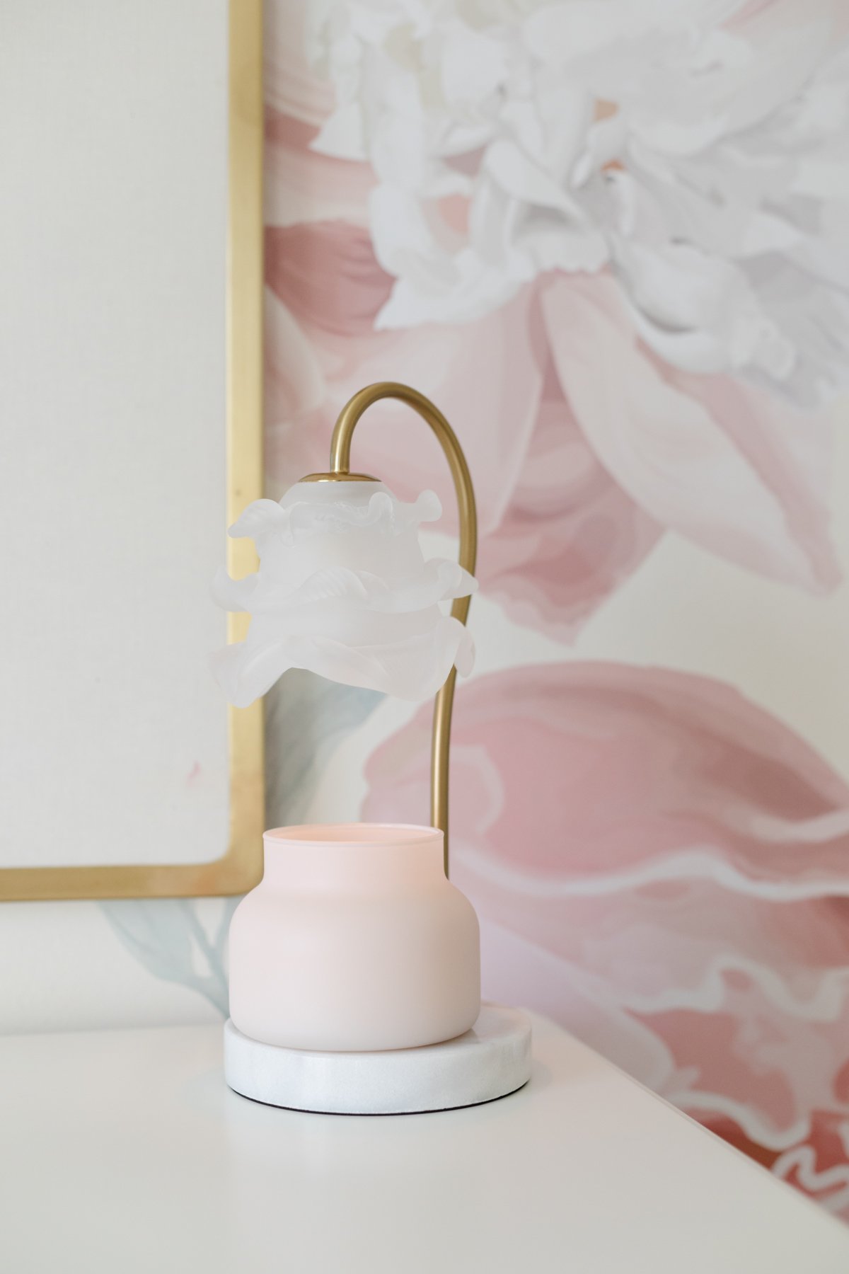 A pink candle warmer lamp on a table next to a pink floral wall.