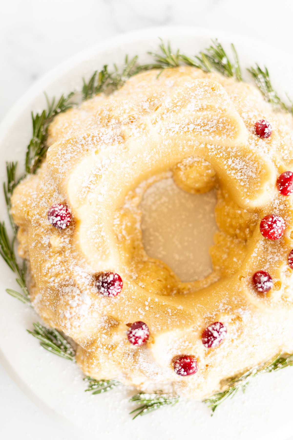 A Christmas bundt cake adorned with cranberries and sprigs of rosemary.