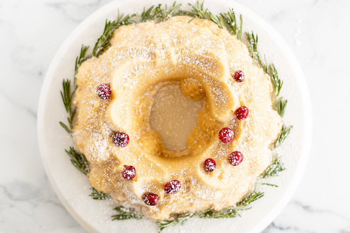 A Christmas bundt cake adorned with cranberries and sprigs of rosemary.