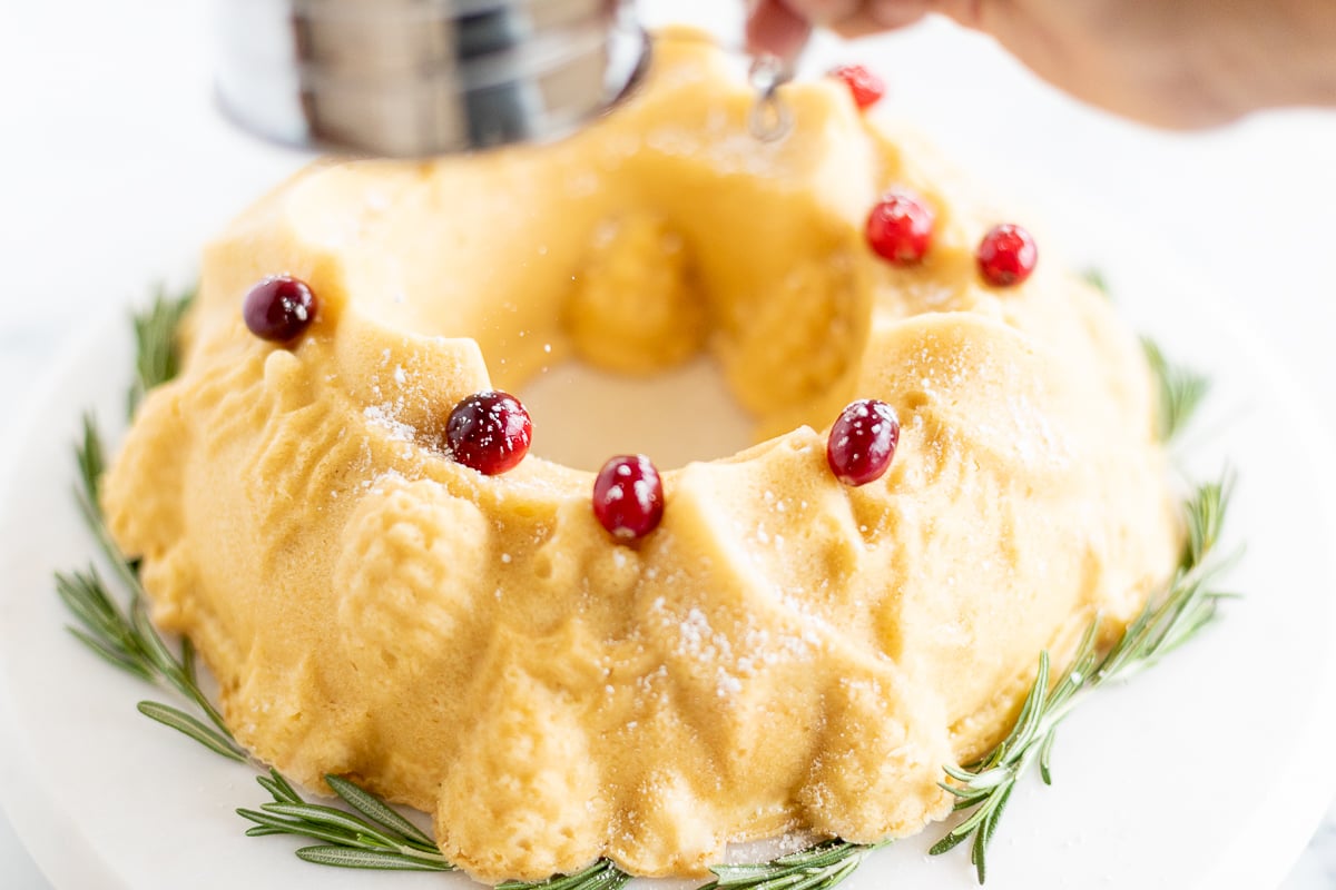 A person is sprinkling sugar on a Christmas bundt cake.