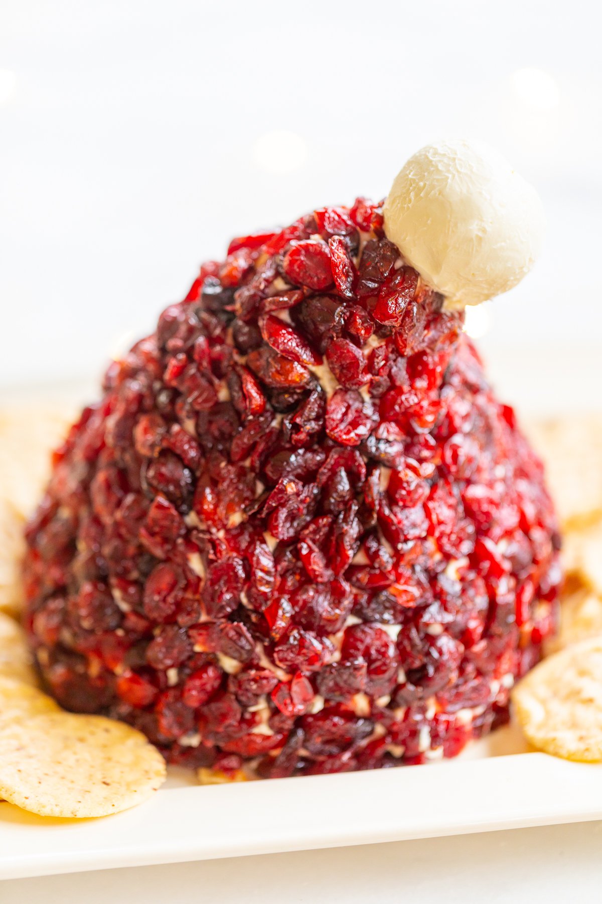 A cranberry cheese ball shaped like a Santa hat, with crackers on a plate.