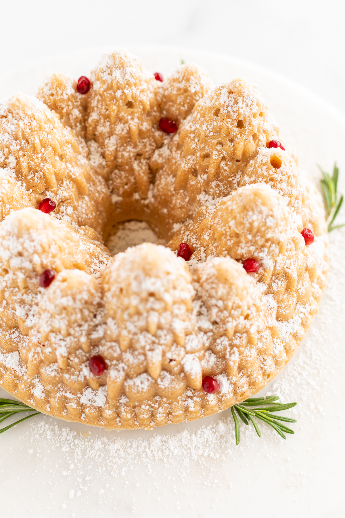 A Christmas bundt cake topped with powdered sugar and a sprig of rosemary.