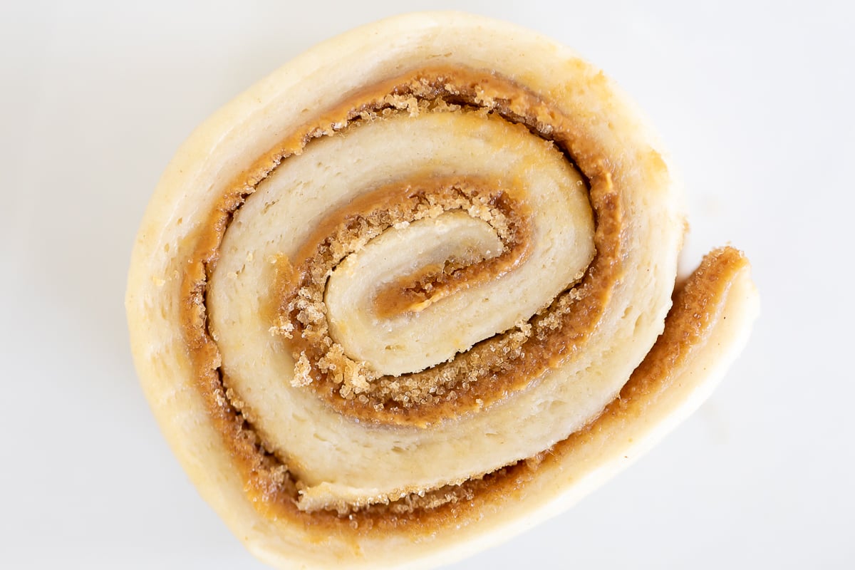 A slice of a Cookie Butter Cinnamon Roll on a white surface.