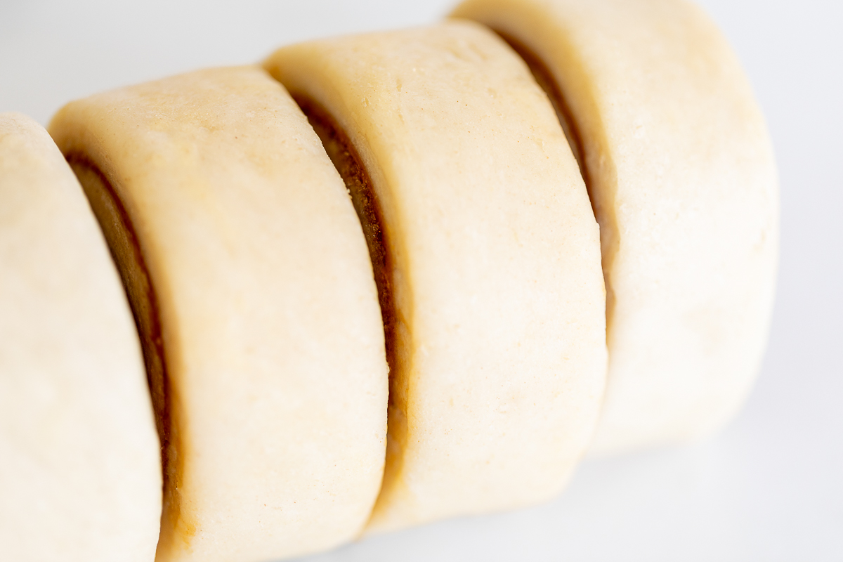 A stack of Cookie Butter Cinnamon Rolls before baking, sliced on a white surface.