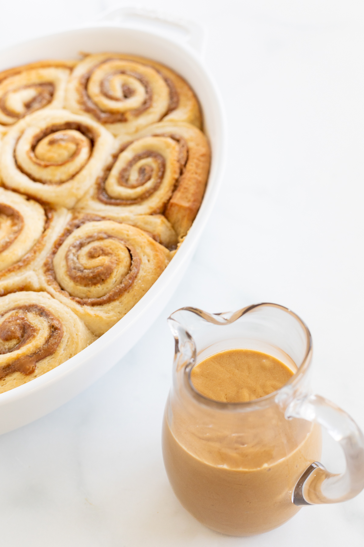 A white dish with Cookie Butter Cinnamon Rolls and a cup of peanut butter.