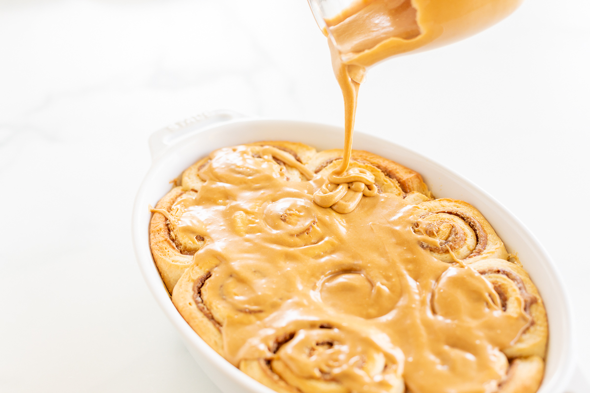 Cookie butter is being poured over a cinnamon roll in a white dish.