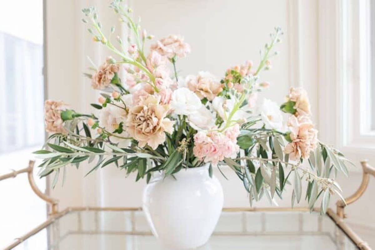 A white vase with pink and white flowers sitting on a Thanksgiving table.