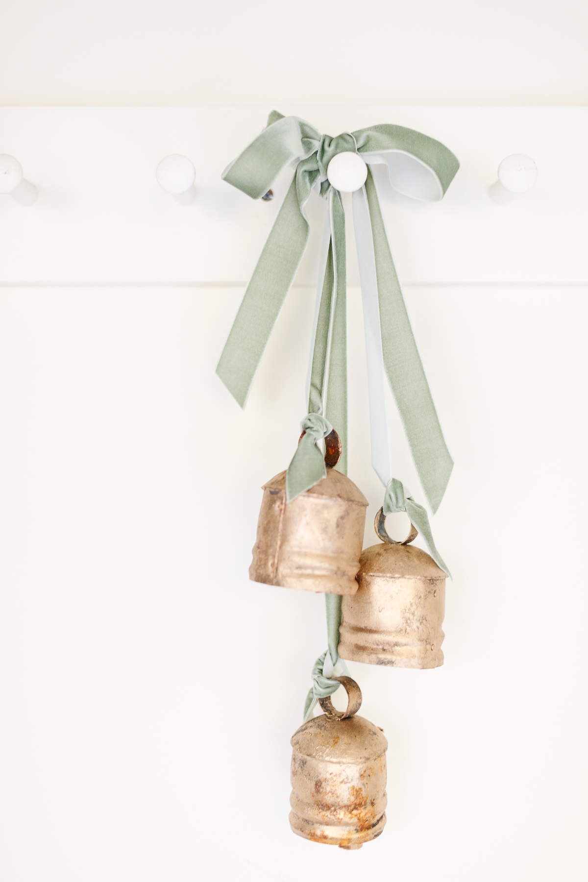Three gold bells hanging on a white wall.