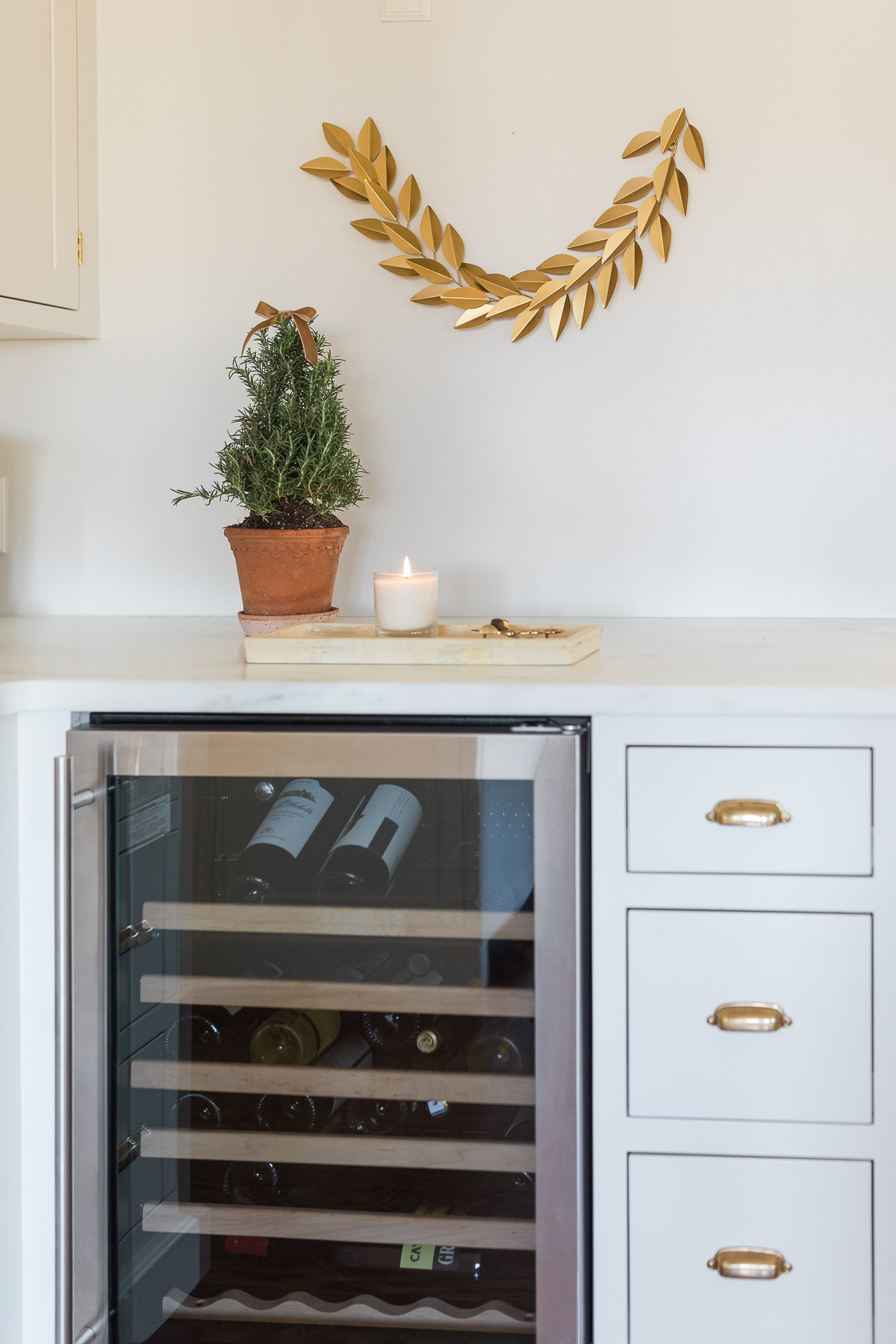A wine cooler in a white kitchen adorned with a gold laurel wreath accent.